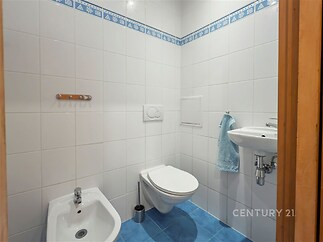 Malá koupelna s modrou dlažbou, bílými obklady a sanitou zahrnuje závěsné WC, umyvadlo a bidet.