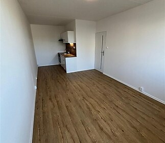 Úzký obývací pokoj s kuchyňským koutem, parketová podlaha, moderní osvětlení, bílá kuchyňská linka, světlé zdi