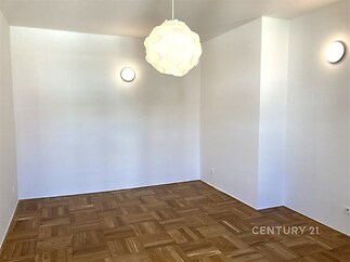Prázdný pokoj s parketovou podlahou a bílými stěnami, moderní stropní svítidlo, dobrý stav, připravený k zařizování.