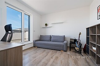 Světlý obývací pokoj s moderní deskou, parketová podlaha, velká okna, minimalistický styl.