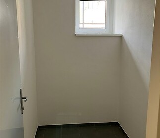 Malý suterénní pokoj s dlažbou a malým oknem. Jednoduchý design, ideální jako úložný prostor nebo prádelna.