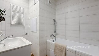 Koupelna s moderní dlažbou, vanou a světlým obkladem, nabízí čistý design a funkční uspořádání.