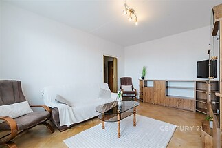 Světlý obývací pokoj s parketovou podlahou, moderním nábytkem a velkými okny, které zajišťují příjemné denní osvětlení.