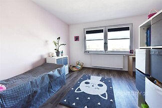 Dětský pokoj s laminátovou podlahou, velkými okny a moderní výzdobou, světlý prostor ideální pro rodinné bydlení.