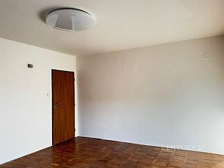 Prázdný pokoj s parketovou podlahou, bílými stěnami a dřevěnými dveřmi, nabízí možnost individuálního zařizování a moderního designu.