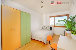 Světlá ložnice s parketovou podlahou, velkým oknem a vestavěnými skříněmi, moderní styl a útulná atmosféra.