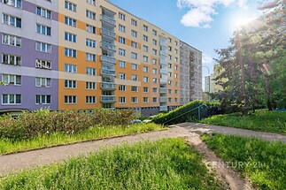 Barevný bytový dům s moderním fasádním designem, dobře udržovaný exteriér se zeleným okolím a přístupovou cestou v klidné lokalitě.