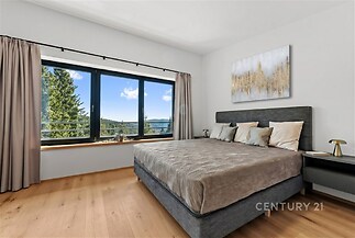Prostorná ložnice s parketovou podlahou nabízí velká okna s výhledem na krajinu, v moderním stylu s neutrálními tóny a elegantní výzdobou.