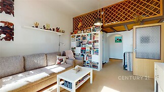 Světlý obývací pokoj s parketovou podlahou, velkým oknem a moderním nábytkem. Vestavěné knihovny a útulný design vytvářejí příjemnou atmosféru.