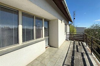 Přístupná terasa s dlažbou a velkými okny, nabízí výhled na okolní krajinu, moderní a útulné v klidné lokalitě.