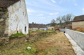 Neudržovaný stavební pozemek s kamenitou zdí a částečně zrekonstruovaným domem, vhodný pro rekonstrukci nebo novou výstavbu.