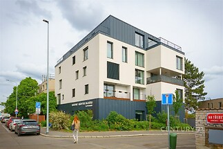Moderní bytový dům s bílou fasádou, velkými okny a prostornými balkony, v klidné části města, ideální pro rodinné bydlení.