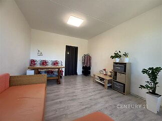 Světlý obývací pokoj s parketovou podlahou, moderní zařízení, velká okna zajišťující dostatek přirozeného světla, světlý interiér.