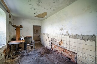 Starý pokoj s opadanou omítkou, poškozenými dlaždicemi a oprýskanými zdmi, vhodný k rekonstrukci, což z něj činí investiční příležitost.