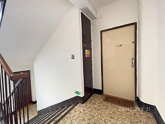 Chodba v bytovém domě s dlažbou, dveře do bytu, schodiště se zábradlím, světlé stěny, dobře udržovaný prostor.