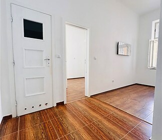 Vstupní předsíň s dřevěnou podlahou, vysoké stropy, světlé stěny, moderní vzhled, přístup do dalších místností, prostorný interiér.