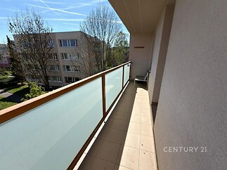 Prostorný balkon s dlažbou a moderním zábradlím nabízí výhled na klidné okolí a vzrostlé stromy, ideální pro relaxaci na čerstvém vzduchu.