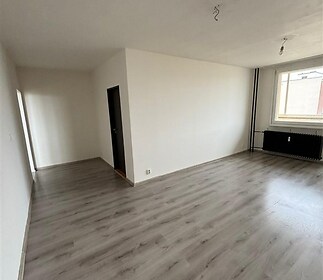 Světlý obývací pokoj s parketovou podlahou, velkým oknem a moderní výmalbou, ideální pro rekonstruované byty a světlé interiéry.