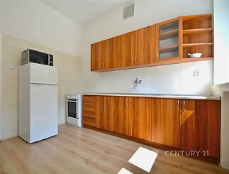 Světlá kuchyň s moderními dřevěnými skříňkami, parketovou podlahou a velkým oknem, které propouští dostatek přirozeného světla.