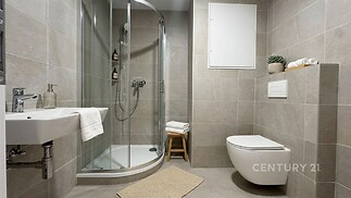 Moderní koupelna s dlažbou, sprchovým koutem a závěsnou toaletou, elegantní design a světlé provedení nabízejí komfort a styl.