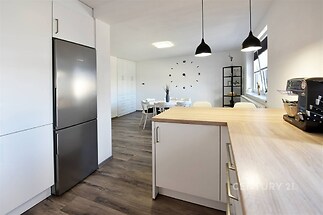 Moderní kuchyň s dřevěnou pracovní deskou, parketová podlaha a vestavěné skříně, světlá jídelna s velkými okny a designovým osvětlením.