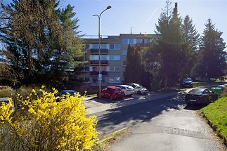 Malý bytový dům s vlastními balkony, obklopený zelení a parkovacími místy, ideální pro klidné bydlení v příjemném prostředí.