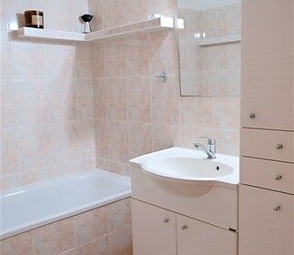 Koupelna s dlažbou, vestavěné skříňky a vanou, nabízí moderní vzhled a praktické úložné prostory.
