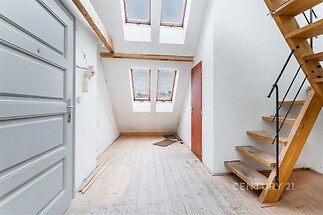 Podkrovní prostor s dřevěnou podlahou, světlý díky střešním oknům, dřevěné schodiště do patra, moderní a vzdušný design.