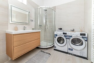 Koupelna s moderní sprchou, dřevěnou skříňkou, světlé dlaždice a pračkou se sušičkou, prostorná a světlá.