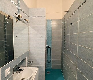 Zrekonstruovaná koupelna s moderními dlaždicemi, sprchovým koutem a elegantním umyvadlem.