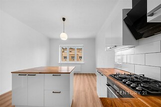 Moderní kuchyň s dřevěnou pracovní deskou, parketovou podlahou a vestavěnými spotřebiči, doplněná velkými okny pro světlý interiér