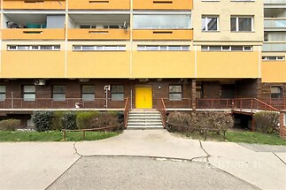 Obytná budova s moderní fasádou, velkými okny a balkony. Rekonstruovaný vchod s rampou pro bezbariérový přístup a udržovaná zeleň.