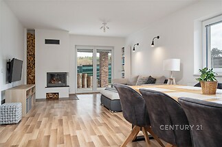 Světlý obývací pokoj s parketovou podlahou, moderní krbová kamna a velká okna nabízejí útulný prostor pro relaxaci.