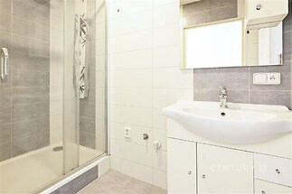 Moderní koupelna s betonovou dlažbou, sprchovým koutem a bílým umyvadlem. Kombinace šedých a bílých obkladů vytváří čistý vzhled.