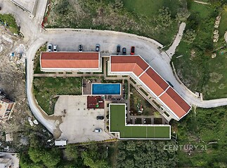 Letecký pohled na moderní bytový komplex s červenou střechou a venkovním bazénem, obklopený zelení, parkovištěm a svěžími zahradami.