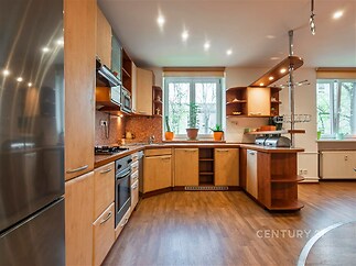 Moderní kuchyň s dřevěnými skříňkami, parketovou podlahou a velkými okny poskytujícími přirozené světlo