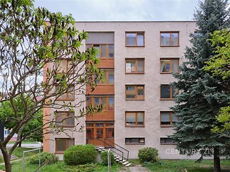Fasáda rekonstruovaného bytového domu s moderními okny, udržovanou zahradou a vstupními dveřmi, obklopená zelení a stromy.