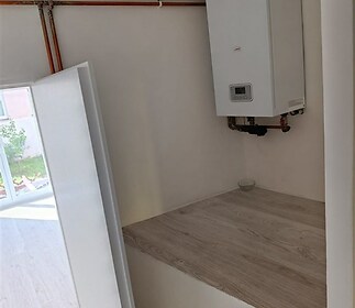 Malá technická místnost s moderním kotlem, dřevěné obložení a světlé stěny, ideální pro úsporné topení v rekonstruovaném domě.