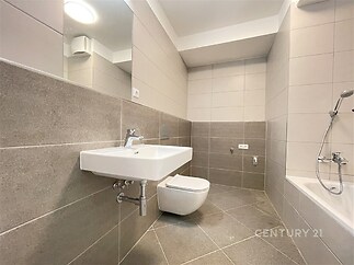 Koupelna s moderními obklady, závěsným umyvadlem a toaletou, dlažba ve světlém šedém tónu, čistý a minimalistický design.