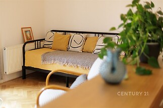 Světlý obývací pokoj s parketovou podlahou, moderním nábytkem a velkými okny vytváří útulnou atmosféru pro relaxaci a odpočinek.