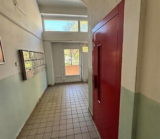 Vstupní hala bytového domu s dlažbou, poštovními schránkami a moderním výtahem, nabízí světlé prostory a funkční design.