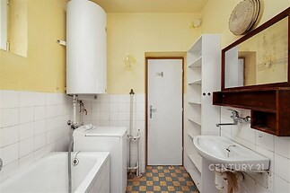 Prostorná koupelna s dlažbou a bílými keramickými obklady, vybavená vanou a umyvadlem, působí jako ideální prostor k rekonstrukci.