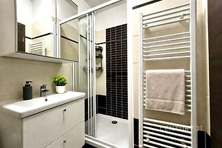 Moderní koupelna s proskleným sprchovým koutem a dlažbou, světlé obklady a designový věšák na ručníky dodávají prostoru stylový vzhled