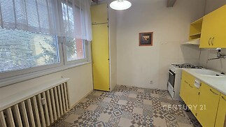 Kompaktní kuchyň s dlažbou s geometrickým vzorem, žlutými skříňkami a plynovým sporákem nabízí praktický prostor pro vaření.