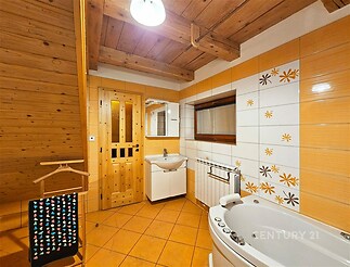 Podkrovní koupelna s dřevěným stropem, dlažbou a rohovou vanou. Světlé obklady s květinovým vzorem dodávají místnosti útulný vzhled.