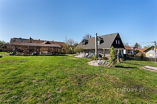 Prostorná zahrada s moderní chatou, dřevěné fasády a kamenné prvky. Obklopena venkovským klidem ideální pro relaxaci a rekreaci.
