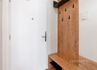 Vstupní hala s dřevěným obložením, moderními háčky a lavicí. Minimalistický design, světlé stěny a čisté linie interiéru.