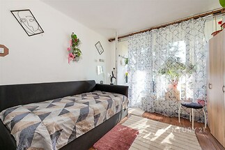 Světlý obývací pokoj s parketovou podlahou, velká okna a moderní závěsy, doplněno dekorativními prvky a světlým interiérem.