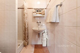 Kompaktní koupelna s dlažbou, sprchovým koutem a moderními obklady. Funkční design a světlé provedení.