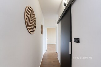 Úzká chodba s moderními prvky, dřevěná podlaha a posuvné dveře. Minimalistický design a dekorativní prvky na stěnách.